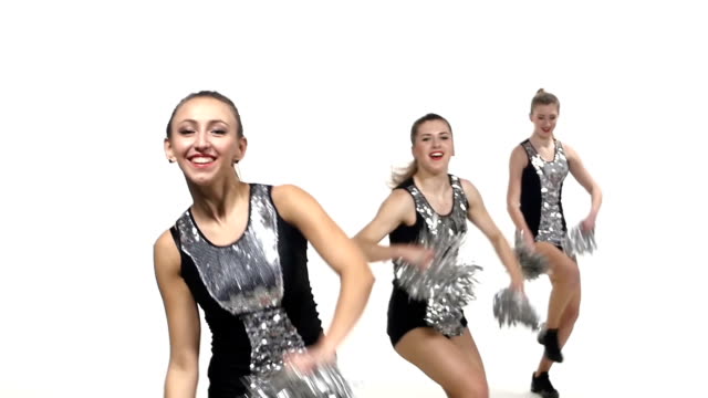 Girls in black costume  with pom-poms dancing on cheerleading competitions, smiling at the camera, slow motion