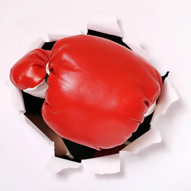 Hand in boxing glove through paper hole. Sport