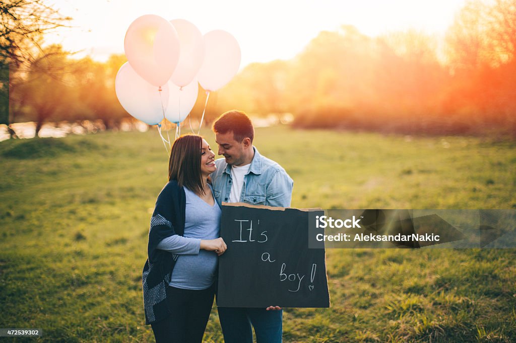 It's a boy Photo of pregnant woman and her man standing on a beautiful meadow and holding ''It's a boy'' board.  Blue balloons next to them. 2015 Stock Photo