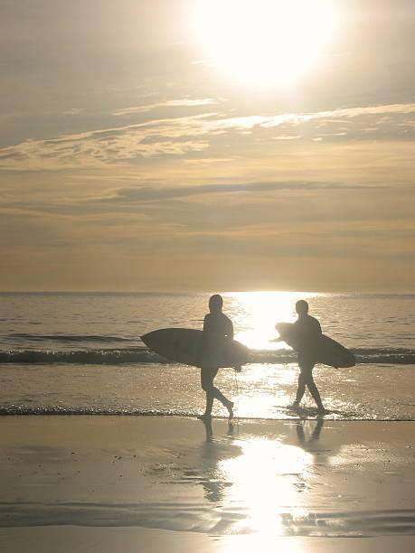 istock Sunset Silhouette of Surfers Walking into Waves 472570102