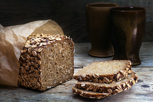 wholegrain rye bread with seeds on a weathered wooden board, rustic earthenware in the dark background