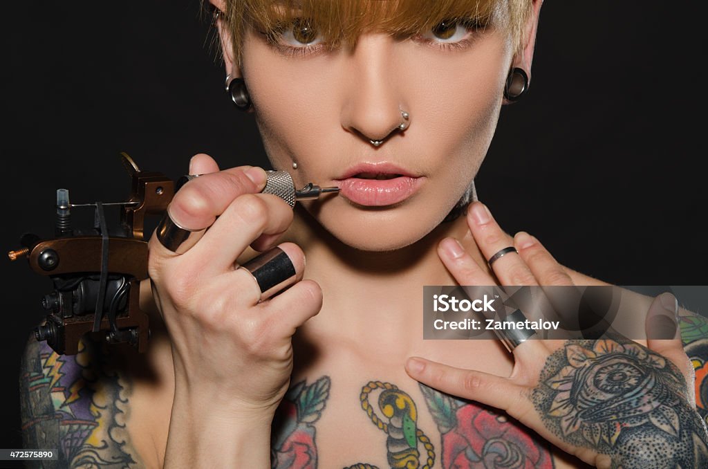 charming blonde with tattoo machine and for them charming blonde with tattoo machine and for them, dark background Tattooing Stock Photo