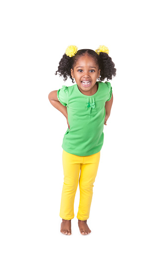 A portrait of an adorable four year old african american girl. She has pigtails with bright yellow flower hair accessories around them. She is smiling and is looking at the camera. She is wearing a green shirt and yellow pants. Shot taken with a Canon 5D Mark 3 camera. rm