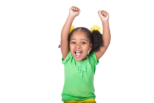 An adorable four year old african american girl has her hands raised in the air. She has pigtails with a bright yellow flower hair accessory around them. She has her mouth wide open and is excited. She is wearing a green shirt.  Taken with a Canon 5D Mark 3. rm