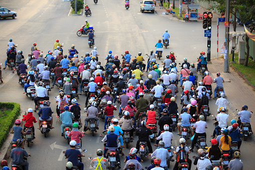 Dense, crowed scene of city traffic in rush hour, crowd of people wear helmet, transport by motorcycle, stop at red light in stress situation, Vietnam