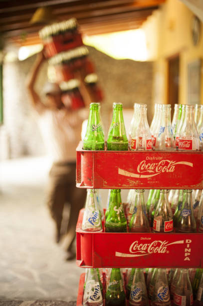 San Pedro la Laguna, Guatemala - January 27, 2011: Local Restaurant in San Pedro la Laguna on lake Atitlan in Guatemala. Delivery man carry Coca Cola glass bottle crates on his shoulder while in focus are the empty bottles in a pile waiting to be collected for recycle use.