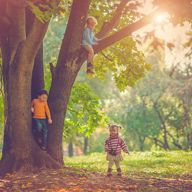 Mom and daughter having fun in autumn forest.They hanging upside down holding with the hands and legs to a large branch of a tree and watch each other. They are very happy. Beautiful nature around them is covered with yellow autumn leaves. Child and mother are wearing colorful handmade sweaters.