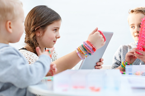 Little kids with digital tablet making loom bands with help of internet