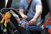 Infant boy in car seat being put in back of car by father