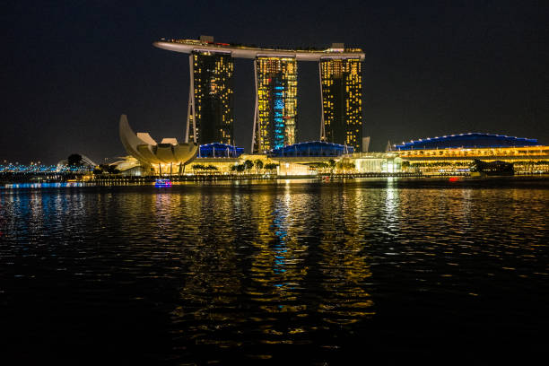 Singapore, Singapore - March 21, 2015: Picture of the Marina Bay Sands hotel in Singapore at night. This is the second most expensive finished building in the world. Picture was taken from far away in the bay where all modern buildings of Singapore are. In front of the hotel a very elegant mall is located. The picture also includes ab blue bridge that connects the two sides of the bay.