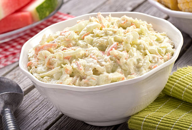 Creamy Coleslaw A bowl of delicious creamy homemade coleslaw on a rustic picnic table with watermelon and corn. coleslaw stock pictures, royalty-free photos & images