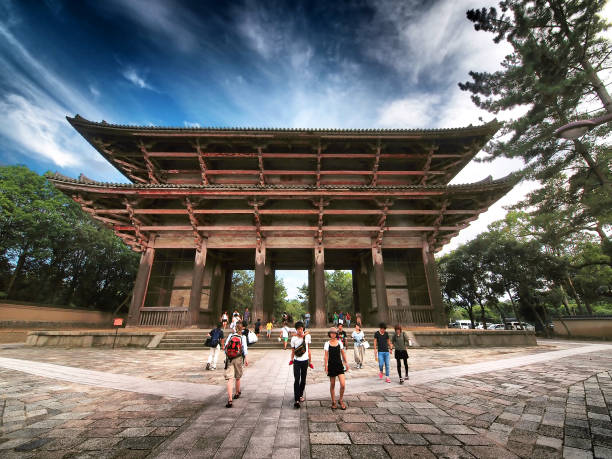 Nara, Japan - August 11, 2014: Front view of Daibutsuden Temple Door in Nara. People, tourists are walking on a path towards the temple door. All around are surrounding park trees and above is dark, dynamic, cloudy sky, it is E5 in camera build HDR filter.