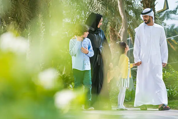 Traditional Middle Eastern family walking in a park on a sunny morning. Mother and father are dressed in traditional clothes. They are talking and having fun. Copy space