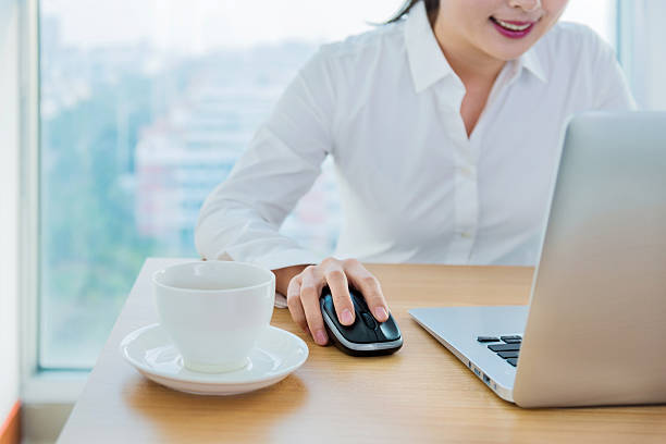 Computer keyboard with mouse and female hands holding cup of coffee