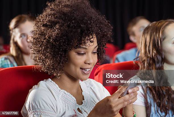 Woman Text Messaging On Her Mobile During Movie Stock Photo - Download Image Now - Movie Theater, 18-19 Years, 20-24 Years