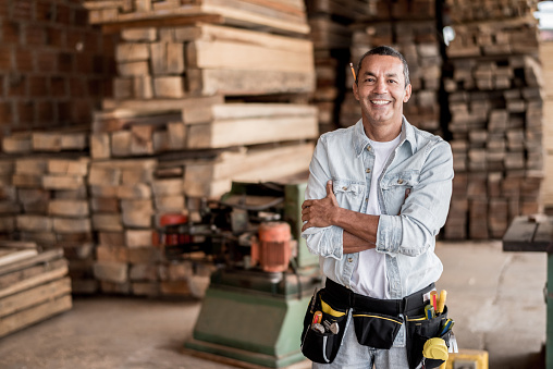 Friendly carpenter at his workshop with piles of wood looking very happy