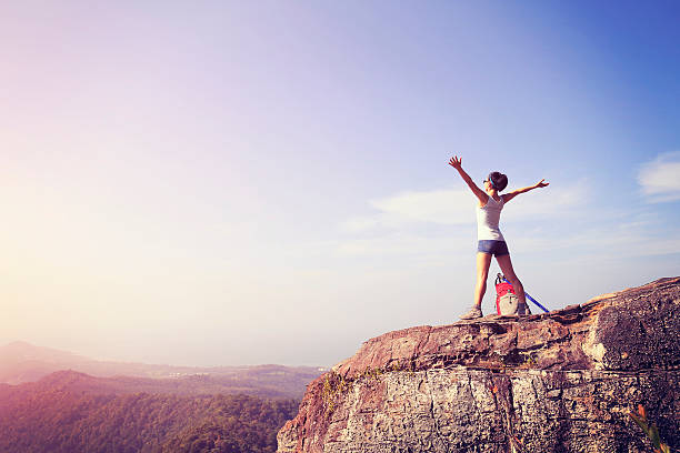istock cheering young woman hiker open arms at mountain peak 472618534