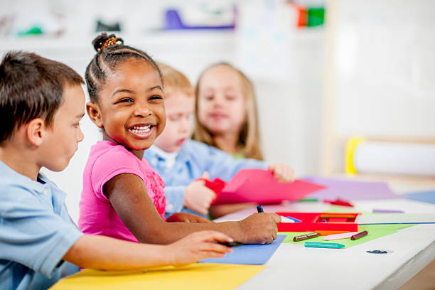 Children Playing at Daycare A multi-ethnic group of preschool age students drawing with crayons in their classroom at school - little girl is smiling and looking at the camera. young children pictures stock pictures, royalty-free photos & images