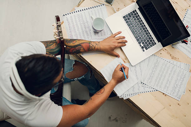 Musician Composing Music. Top view of an man with acoustic guitar composing music for iStock and Getty stock library. Using laptop and writing lyrics or music notes. music sheet tattoo stock pictures, royalty-free photos & images