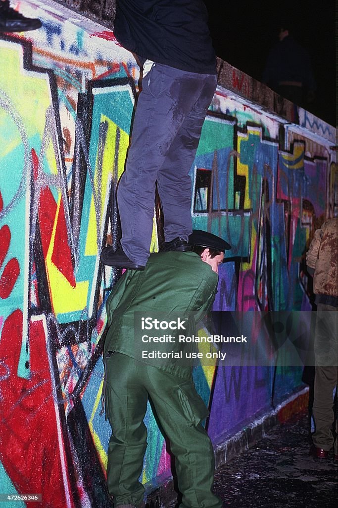 Fall of the Berliner wall in 1989 Berlin, Germany - November 9, 1989: The night of the of the wall in Berlin. People from West Berlin are climbing on the wall at the Pariser Platz, where the Brandenburger Tor is located. In these picture a policeman is helping a person to get on the wall. A very historivcal momemt. "These is a scanned film" Brandenburg Gate Stock Photo