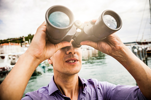 Man looking through binoculars on a pier during a vacation.