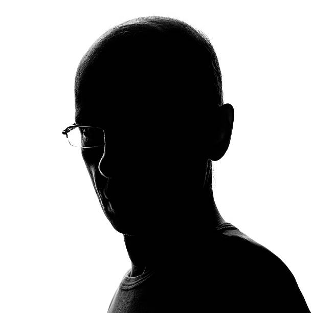 Head and Shoulders Man's Silhouette A man wearing glasses in a head and shoulders 3/4 position against bright light. The man's face is in deep shadow and only his contour is illuminated from the light coming from behind. high contrast stock pictures, royalty-free photos & images