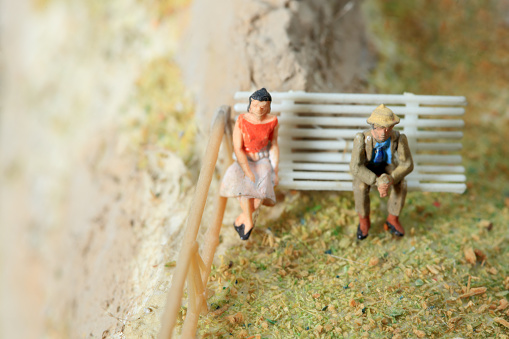 Miniature figurine couple sitting separated on a park bench.