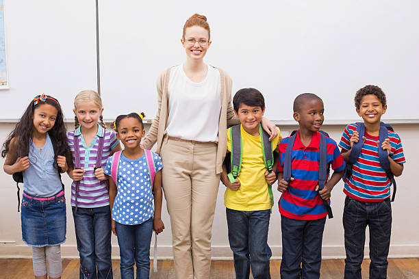 istock Teacher and pupils smiling at camera in classroom 472662562
