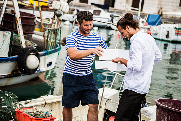 Fisherman passing fish boxes to a waiter on the fish boat moored at the harbor.