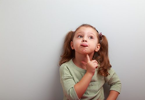 Fun grimacing girl thinking and looking up on blue background with empty copy spase