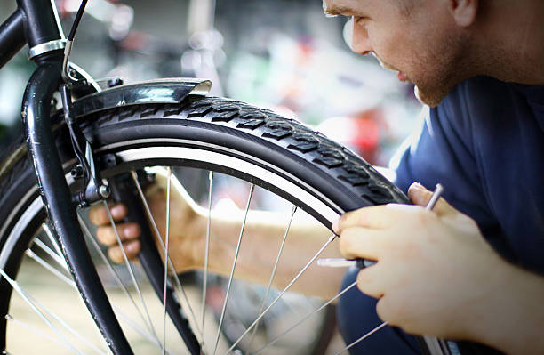 Bike mechanic repairing a wheel Mid-aged caucasian man making sure that the front wheel is aligned and balanced.Also checking if the brake is ok.Usual daily routine in bike workshop.He's wearing navy blue sweater. chainring stock pictures, royalty-free photos & images