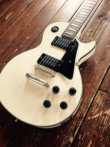 Detroit, MI - May 6, 2015: Vintage Les Paul style electric guitar in a white finish with a distressed hardwood floor in the background.