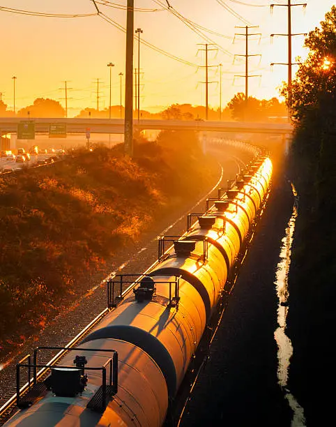 Tank cars of a long freight train glow orange in the light of the rising sun