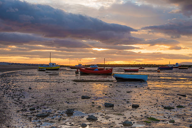 Beached boats at Morecambe Bay, Lancashire, England on a warm late spring evening.  The tide is out and a storm laden sky is gathering as the sun sets.