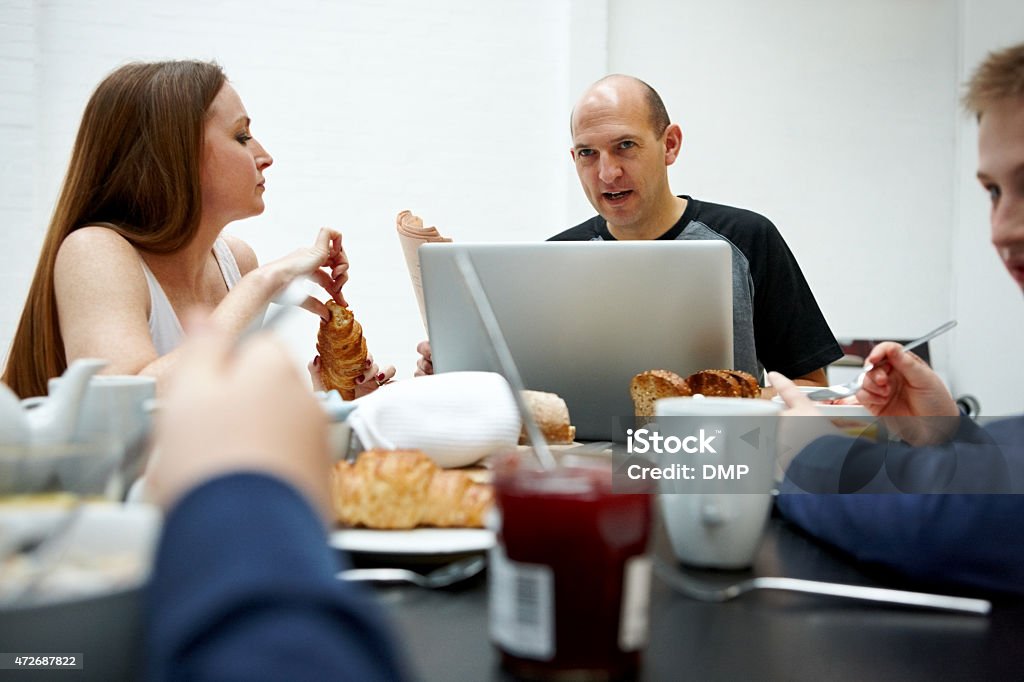 Man using laptop while having breakfast with family Man using laptop while having breakfast with his family - Morning routine 2015 Stock Photo