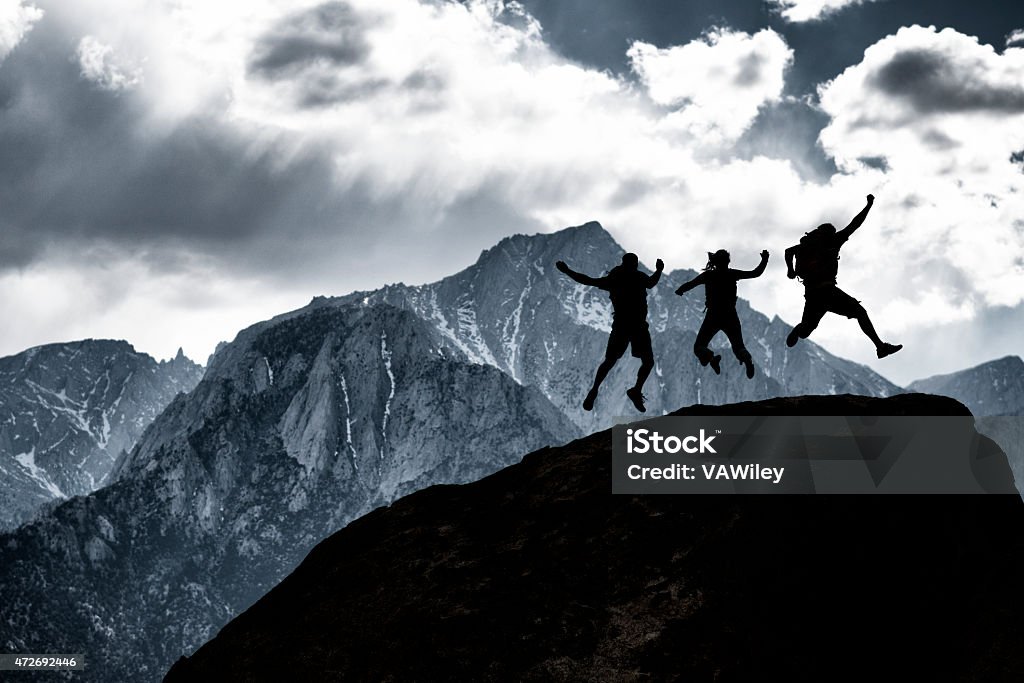 Three friends three friends jumping for jot with a huge mountain behind them  2015 Stock Photo