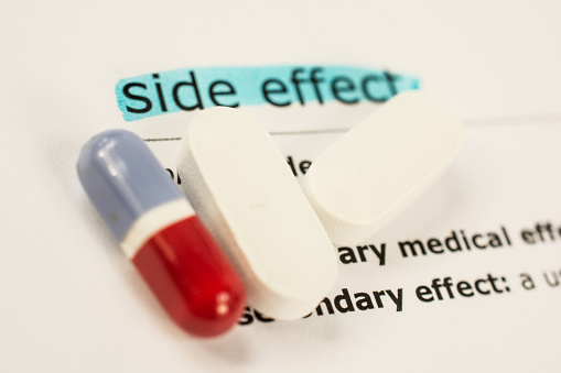 Colored pill and capsules on sheet of medicinal side effects-white background.