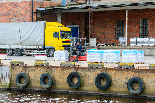 Karlshamn, Sweden - May 06, 2015: Unknown male forklift driver making a phonecall while unloading pallets at the docks. Truck and building in background.
