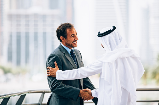Emirati man and western businessman having outdoors meeting. They having agreement and handshaking.
