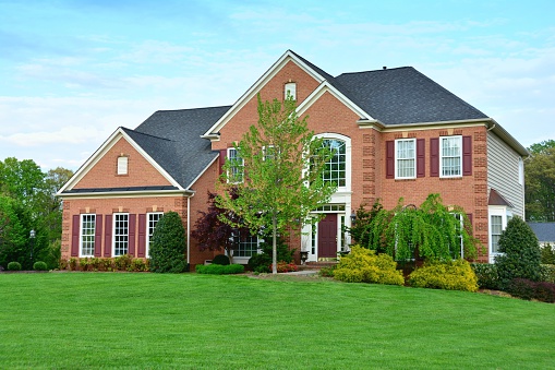 Photograph of a modern brick home with blooming landscaping and green grass.
