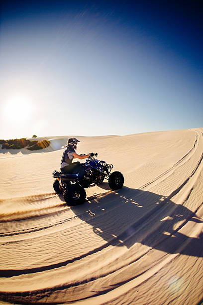 istock Quad biker driving up sand dune on hot summer day 472707910