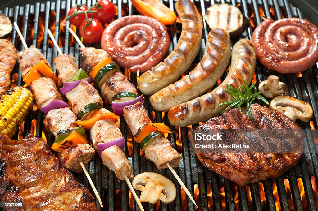 Various cooking meats on a flame grill Assorted delicious grilled meat with vegetable over the coals on a barbecue Barbecue - Meal Stock Photo