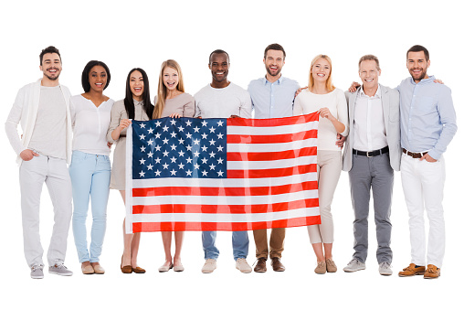 Full length of happy diverse group of people bonding to each other and holding flag of America while standing against white background together
