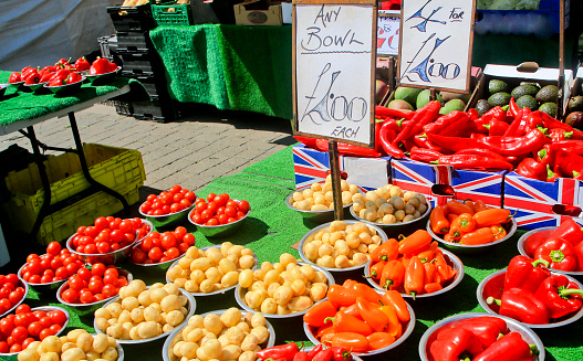A table of red tomatoes, white potatoes and red peppers in a outdoor farmers market in Loughborough, Leicestershire, UK. The Prices are on large posters.