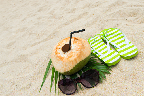 Pair of green striped sandal, sunglasses and coconut on the beach