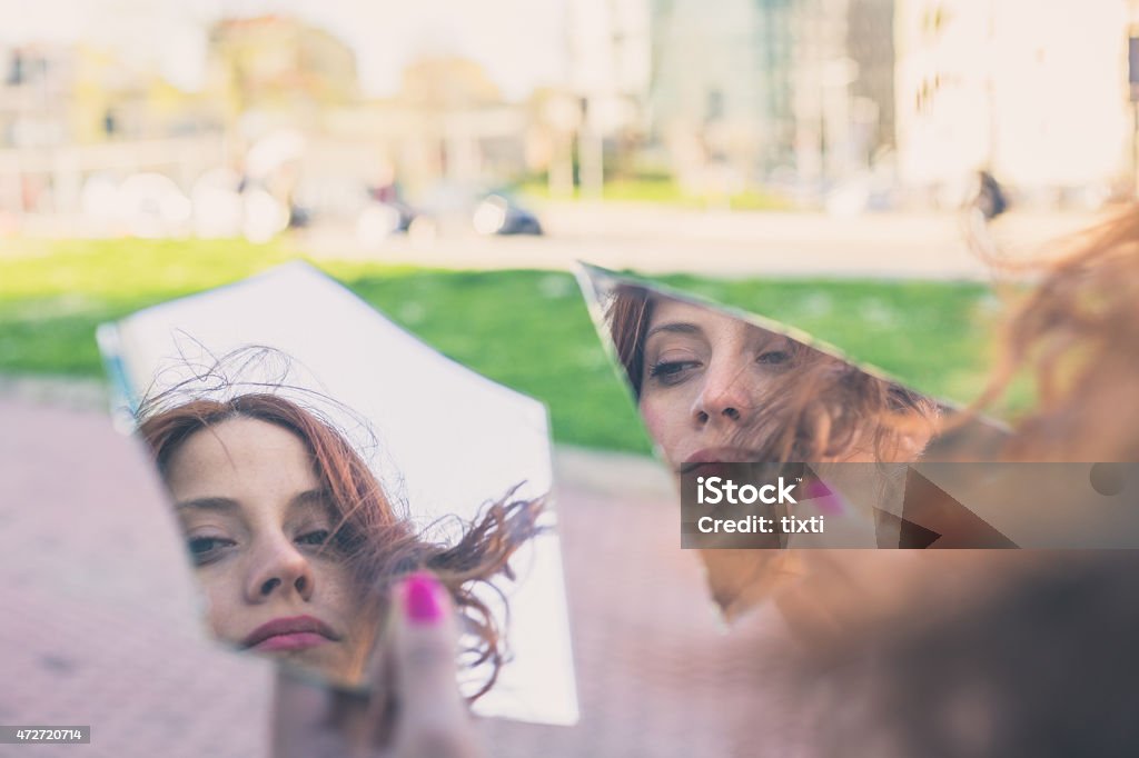 Beautiful girl posing in the city streets Beautiful redhead girl with long hair and blue eyes looking at herself in a broken mirrorBeautiful redhead girl with long hair and blue eyes posing in an urban context Broken Stock Photo