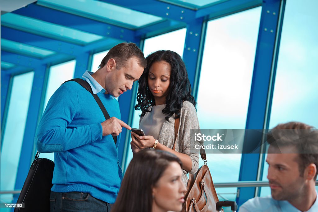 People at the airport lounge using smart phone Afro american woman and caucasian man using smart phone at the airport lounge with blured two people in the foregorund. 2015 Stock Photo