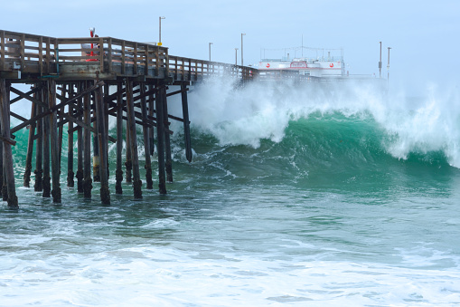 Newport Beach, USA - May 4, 2015: A huge wave crashes through the pillars of Balboa pier on Monday, May 4, sending spray high in the air.  The unusually high surf was fueled by a storm in the southern hemisphere.