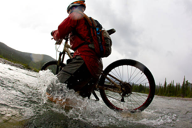 A man carries his bike while crossing a river in a long distance mountain bike race on a rainy day.