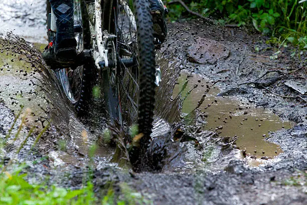 A man competing in a mountain bike race rides through a deep puddle on a muddy trail.